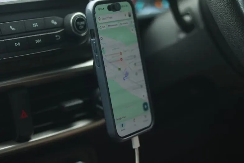 Automobilio salone prie oro ventiliacijos grotelių pritvirtintas išmanusis telefonas. Telefono ekrane atidaryta navigacijos programėlė.