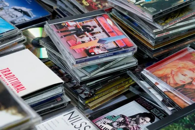 Ant paviršiaus sudėta daugybė kompaktinių diskų dėžučių. Matyti įvairių muzikos albumų viršeliai ir keli CD diskai, sukrauti į kelias krūvas.