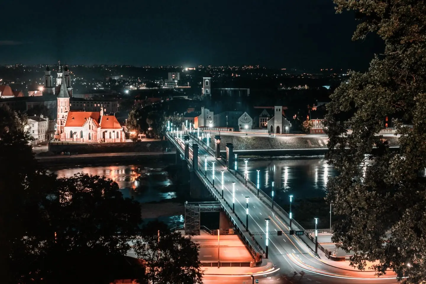 Naktinis Kauno miesto panoramos vaizdas su apšviestu tiltu per upę.