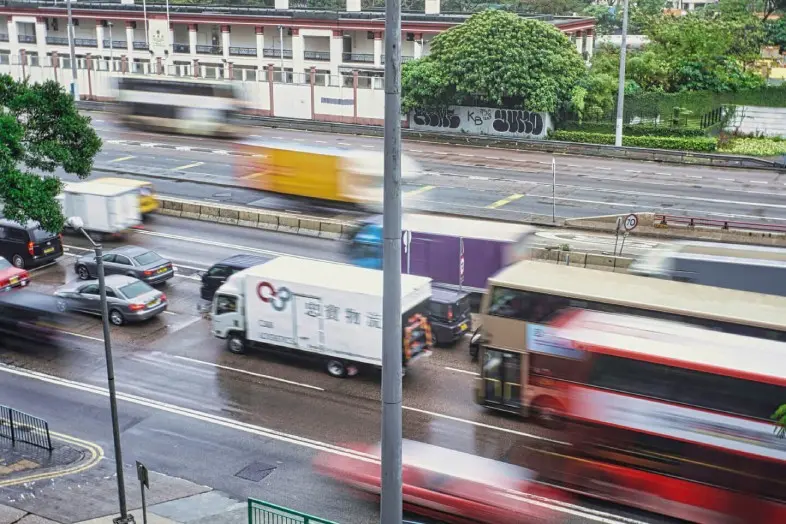 Eismas miesto gatvėje po lietaus. Keliose eismo juostose važiuoja autobusai, sunkvežimiai ir automobiliai, dalis transporto priemonių sulietos dėl judėjimo.