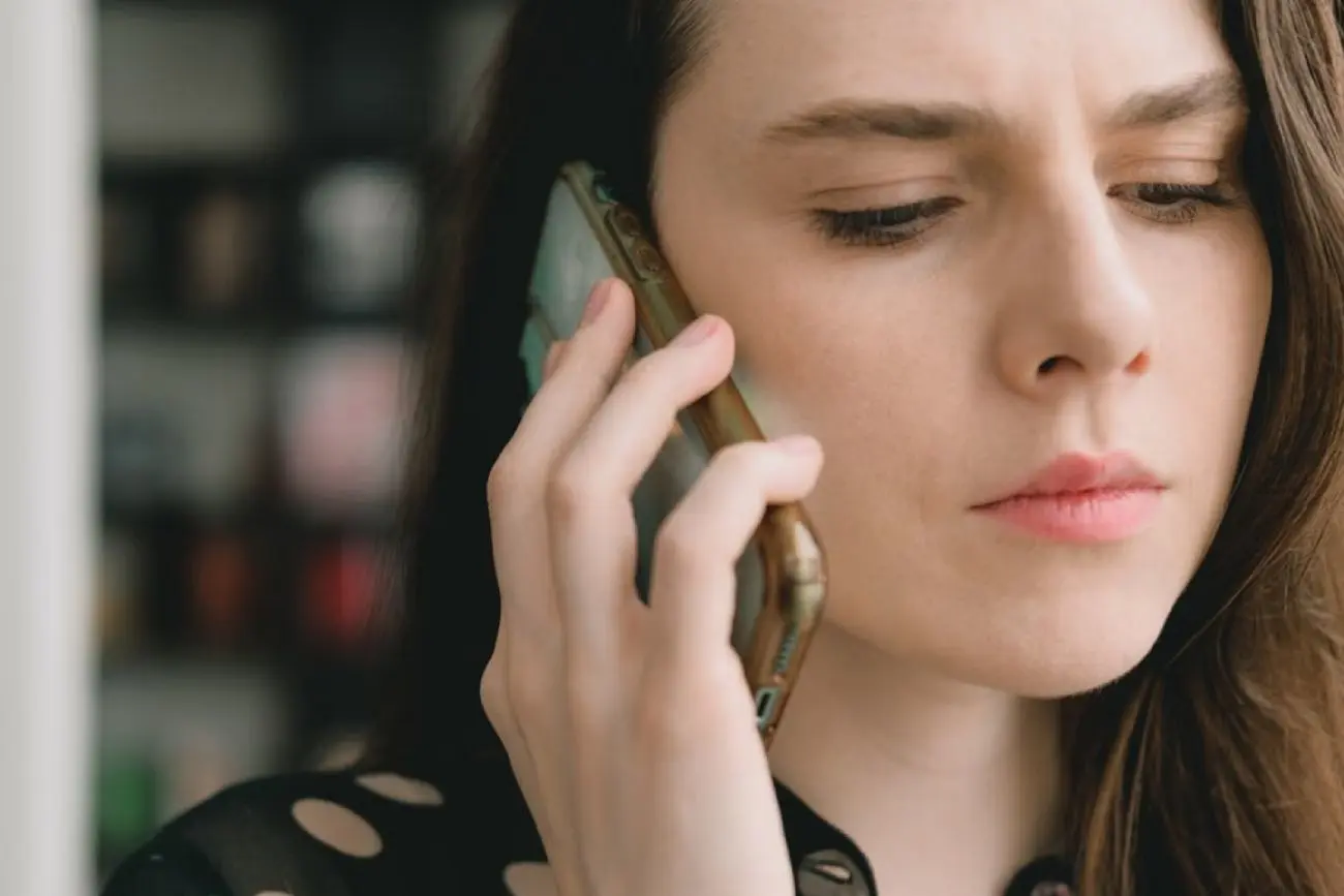 Moteris įdėmiai klausosi prie ausies pridėto mobilaus telefono.