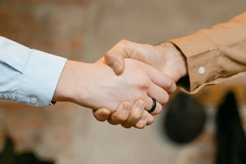 Stambiu planu pavaizduotas dviejų žmonių rankų paspaudimas.