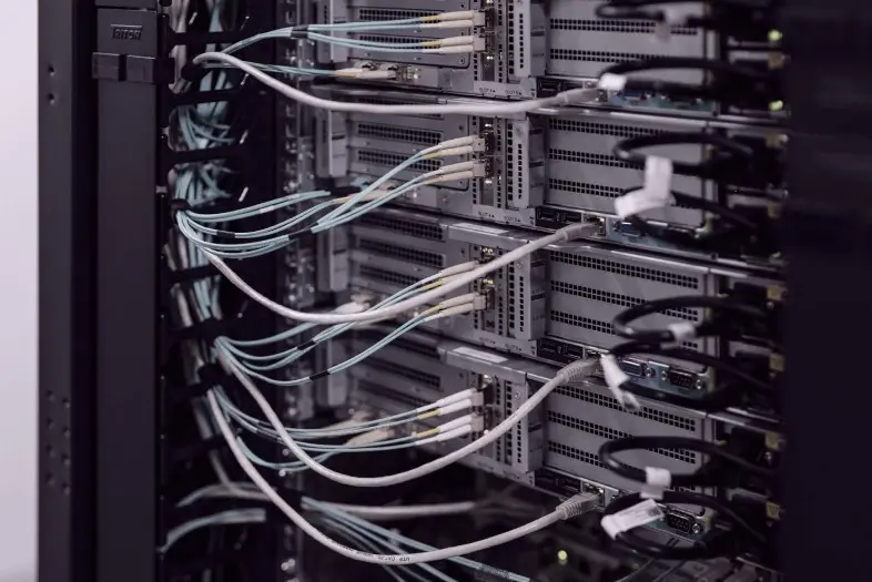 Duomenų centro serveriai su prijungtais tinklo kabeliais. Matoma techninė infrastruktūra, skirta duomenų saugojimui ir tinklo veikimui.