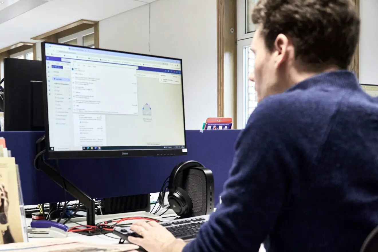 Vyras dirba prie kompiuterio biure ir peržiūri elektroninio pašto bei darbo įrankių informaciją monitoriuje.