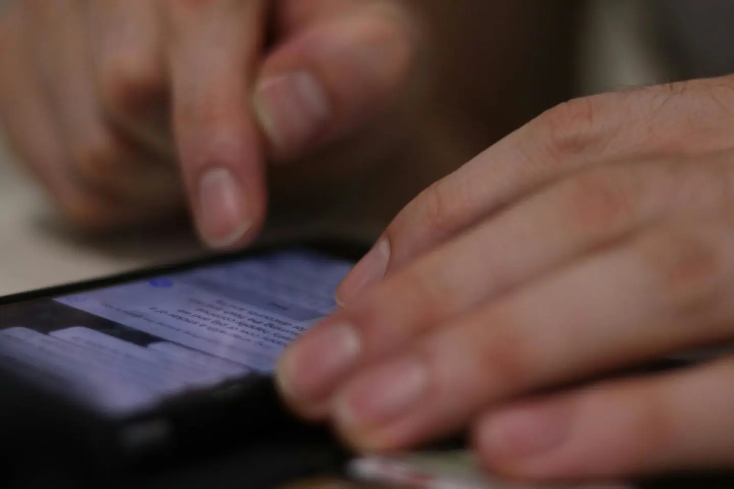 Pirštai spaudžia telefono ekraną rašant arba skaitant žinutę.