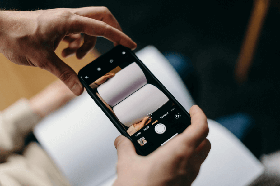 Dviem rankomis laikomas išmanusis telefonas fotografuoja atverstą knygą.