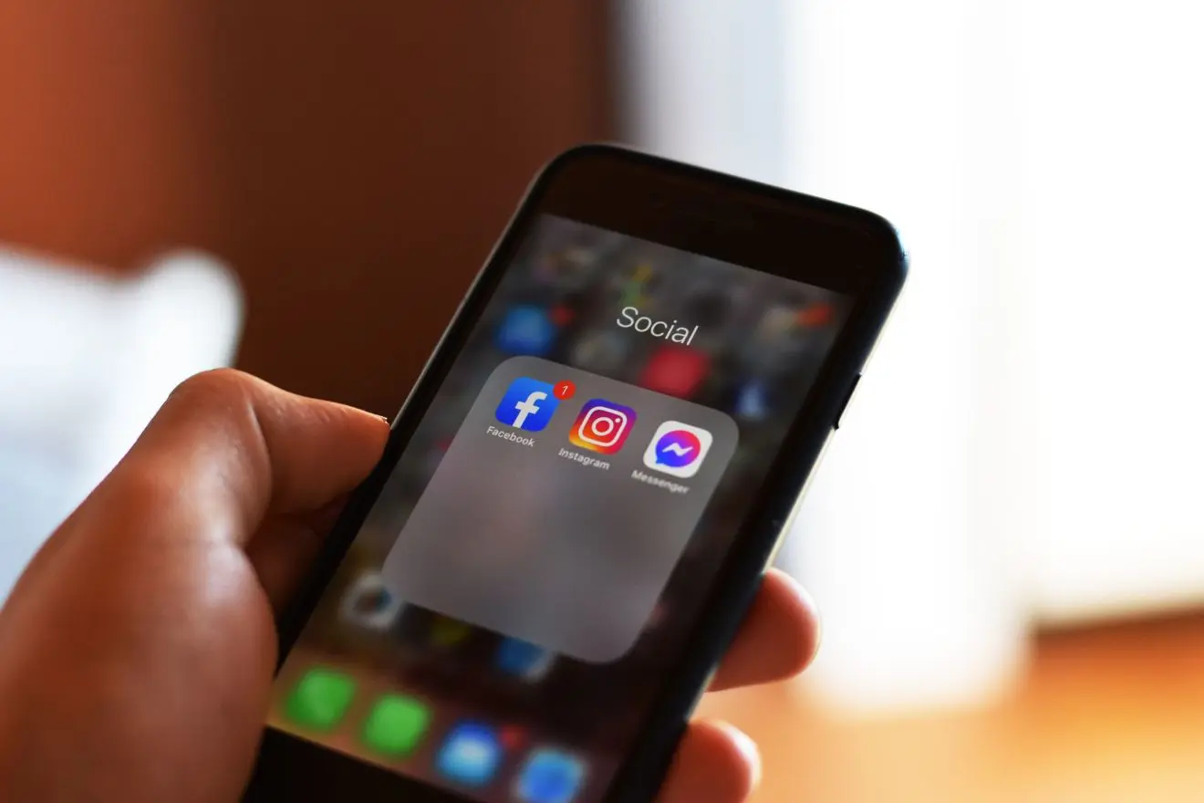 Rankoje laikomas išmanusis telefonas. Jo ekrane matomos socialinių tinklų ikonos.