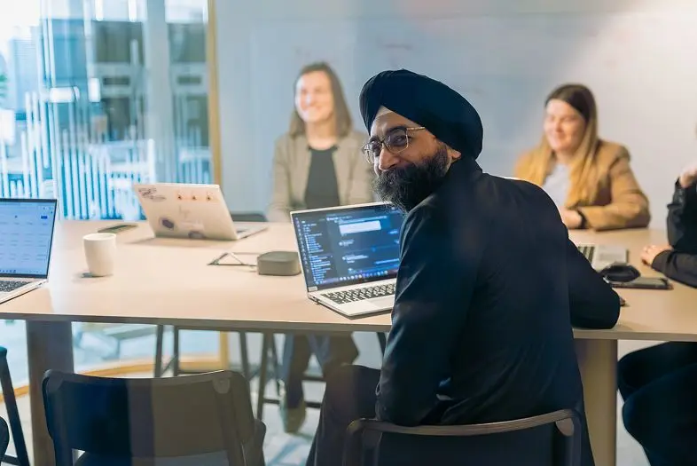 IT architektas Darshanjeet Singh Sachdeva su kitais komandos nariais sėdi prie stalo susitikimų kambaryje.