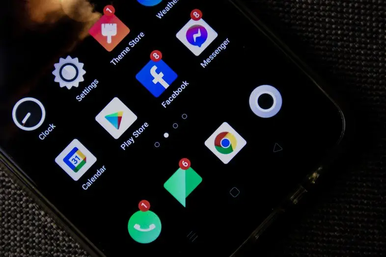Priartintas išmaniojo telefono pradžios ekranas su socialinių tinklų, naršyklės ir sistemos programėlių piktogramomis. Kai kurios programėlės turi neperskaitytų pranešimų indikatorius.