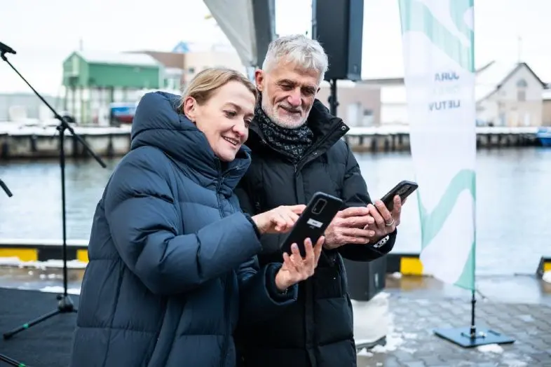 Telia Lietuva vadovė Giedrė Kaminskaitė-Salters su Klaipėdos valstybinio jūrų uosto direkcijos generaliniu direktoriumi Algiu Lataku stovi Klaipėdos uoste, žiūri į telefoną ir kalbasi.