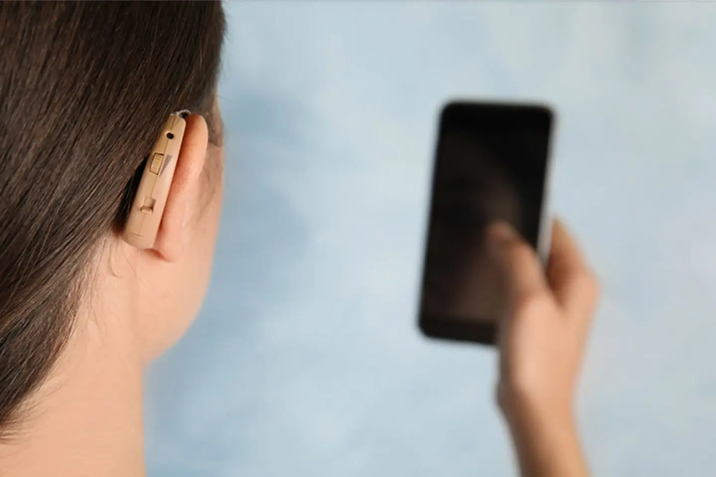 Mergina su klausos aparatu laiko mobilųjį telefoną rankoje