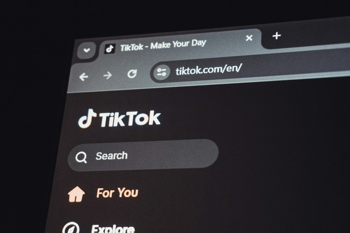 Kompiuterio ekrane atidaryta „TikTok“ svetainė. Matomas platformos logotipas, paieškos laukelis ir naršymo meniu su skiltimis „For You“ ir „Explore“.