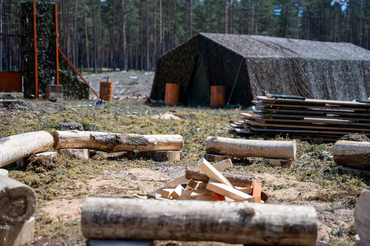 Miško stovyklavietė su maskuojama palapine ir rąstų laužaviete