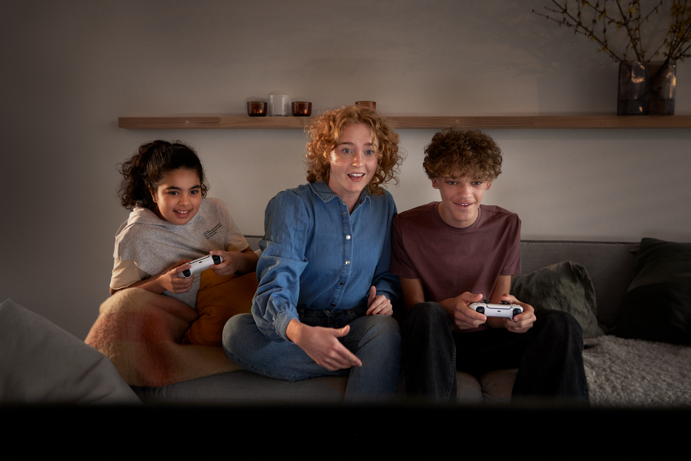 Trys žmonės žaidžia su konsole ir žiūri į TV ekraną