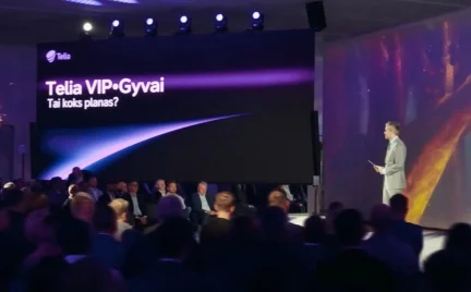 „Telia VIP Gyvai“ renginio scena su pranešėju ir auditorija. Dideliame ekrane rodoma žinutė „Tai koks planas?“, scena apšviesta violetine šviesa.