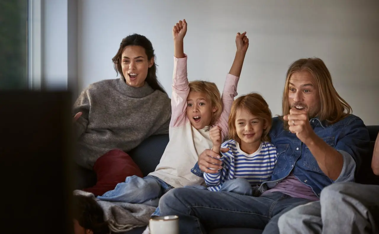 Mama, tėvas ir du vaikai linksmai žiūri televiziją