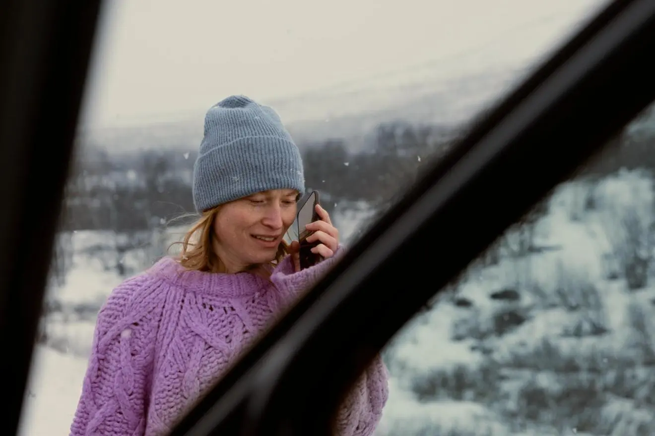 Moteris skambina telefonu snieguotoje aplinkoje