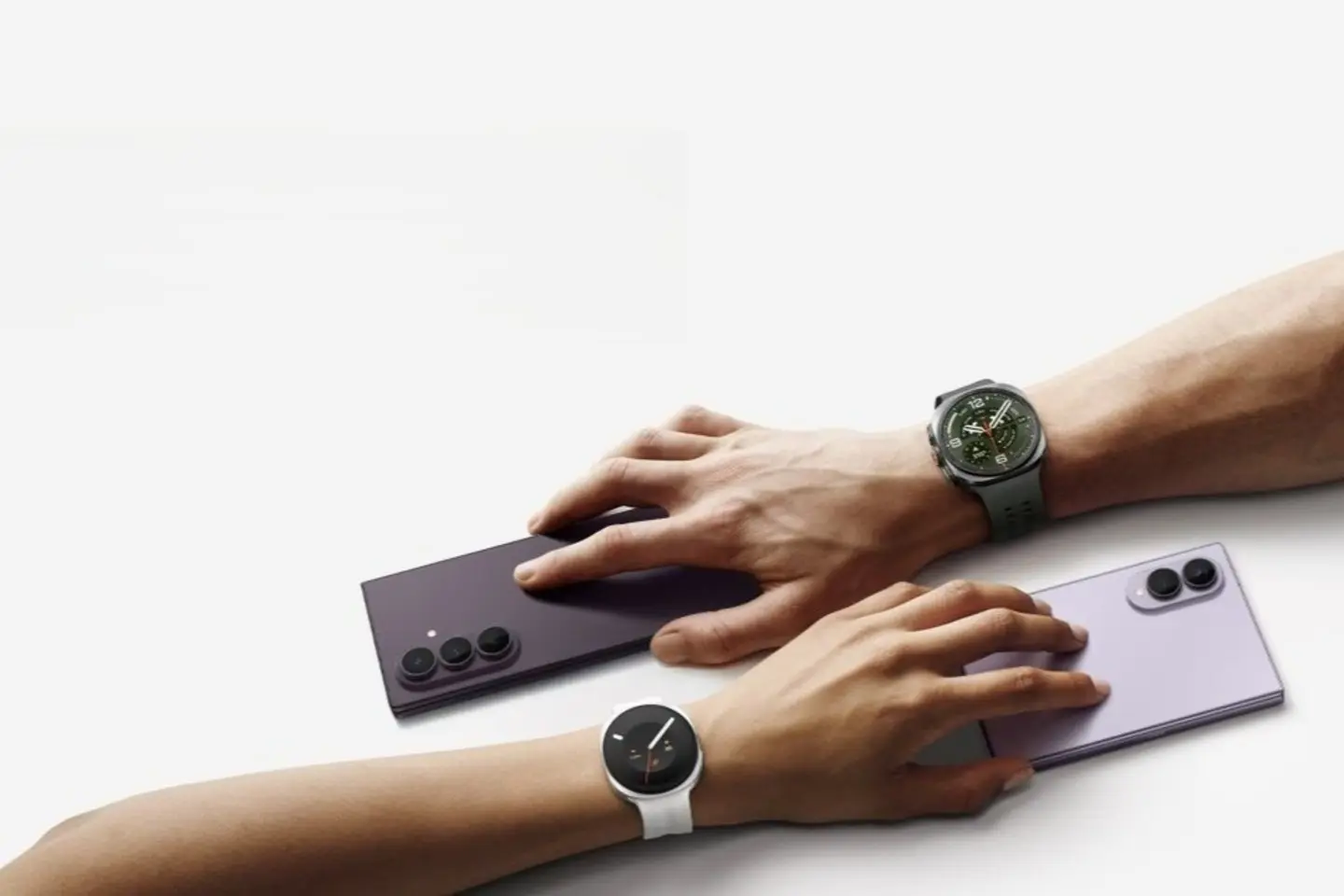 Ant šviesaus fono dvi rankos: viršutinė laiko šešėlių violetinį „Galaxy Fold8 Ultra“ ir dėvi titano sidabro „Galaxy Watch Ultra2“; apatinė laiko levandų violetinį „Galaxy Fold8“ ir dėvi kreminį „Galaxy Watch9“