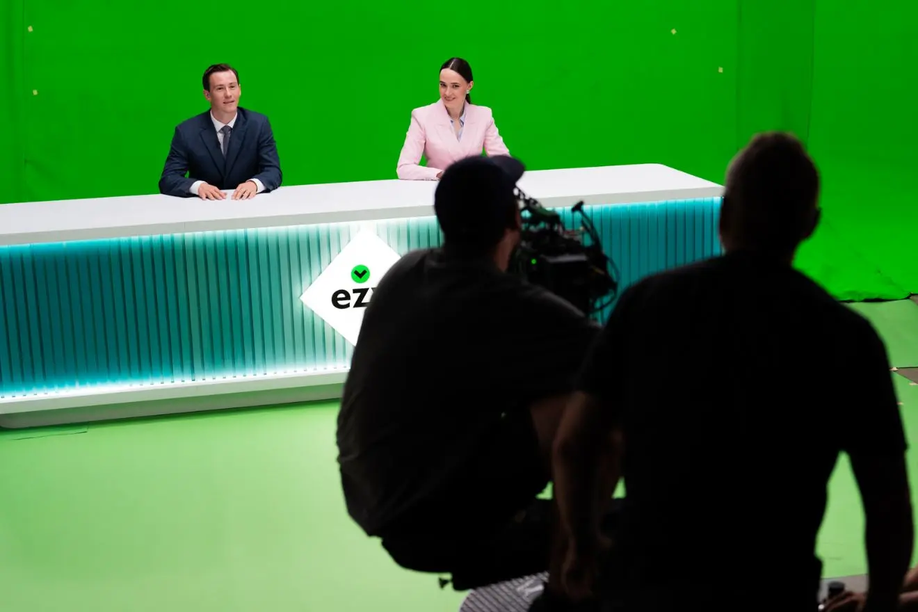 Filmavimo komanda dirba studijoje prie reklamos projekto. Fone matomas žalias ekranas, o centre vyksta įrašo filmavimas.