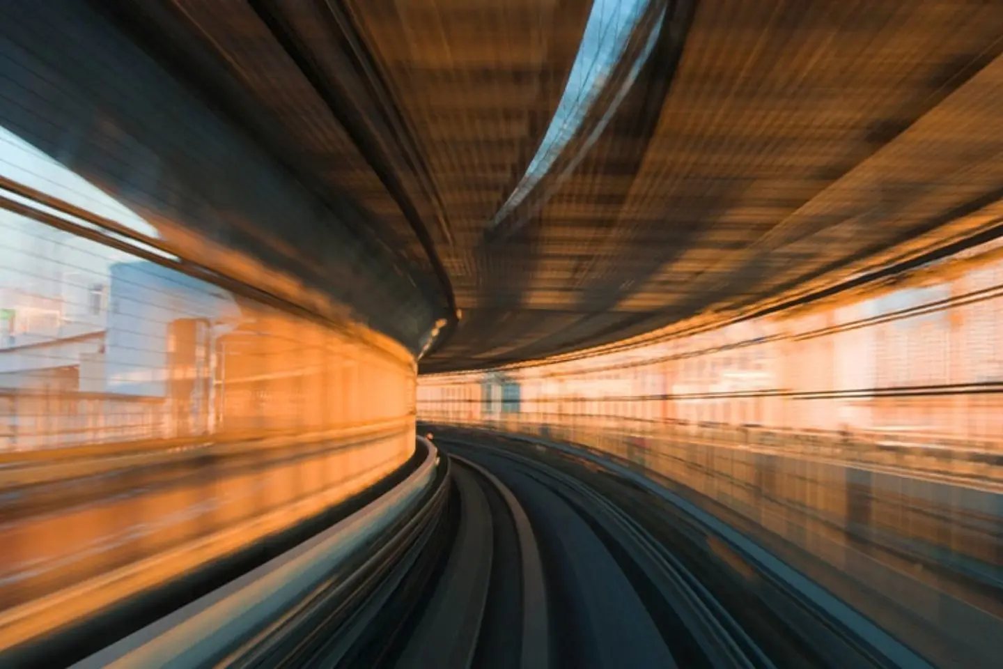 Greitai judančio transporto vaizdas tunelyje ar stotyje. Sulietos linijos ir šiltos šviesos pabrėžia greitį bei modernią infrastruktūrą.