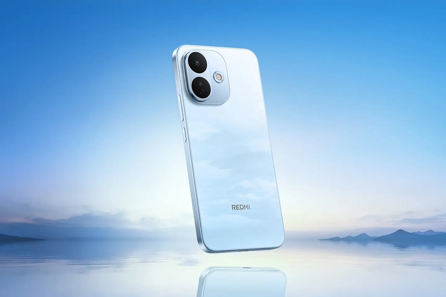 Šviesiai mėlynas „Redmi“ išmanusis telefonas rodomas iš nugarėlės. Matomas dviejų kamerų modulis, o fone atsispindi ramus vandens ir kalnų peizažas.
