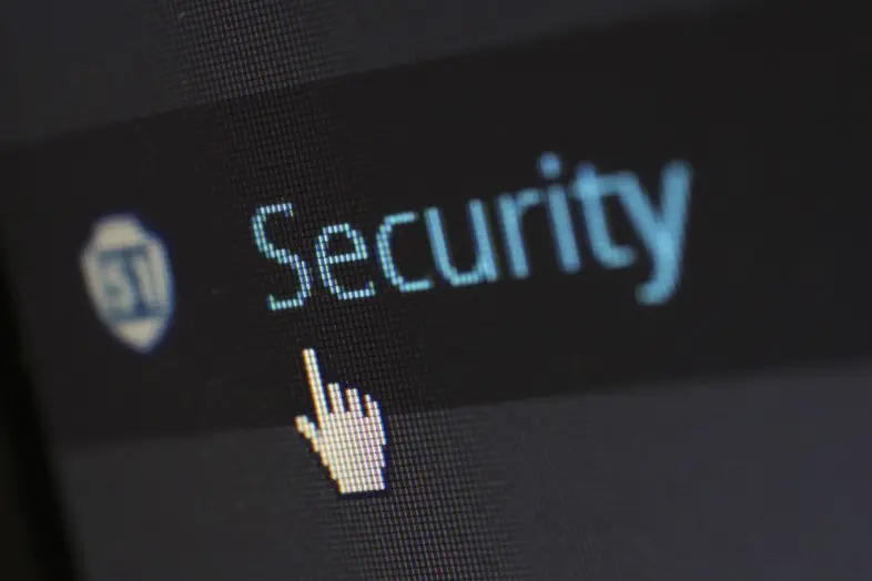 Kompiuterio ekrano stambus planas su užrašu „Security“ (lietuviškai - Saugumas). Šalia matomas skydo simbolis ir pelės žymeklio ranka, nukreipta į saugumo nustatymus.