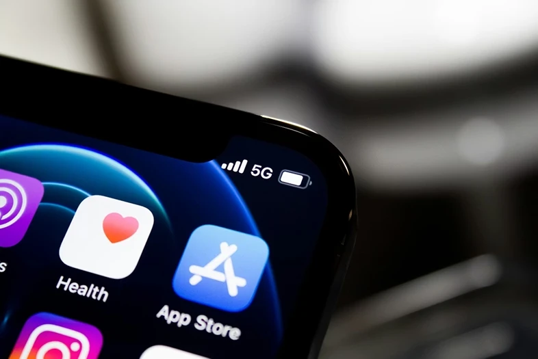 Iš arti nufotografuotas išmaniojo telefono ekrano kampas. Viršuje matoma 5G ryšio piktograma, o ekrane rodomos „Health“ ir „App Store“ programėlių ikonėlės.